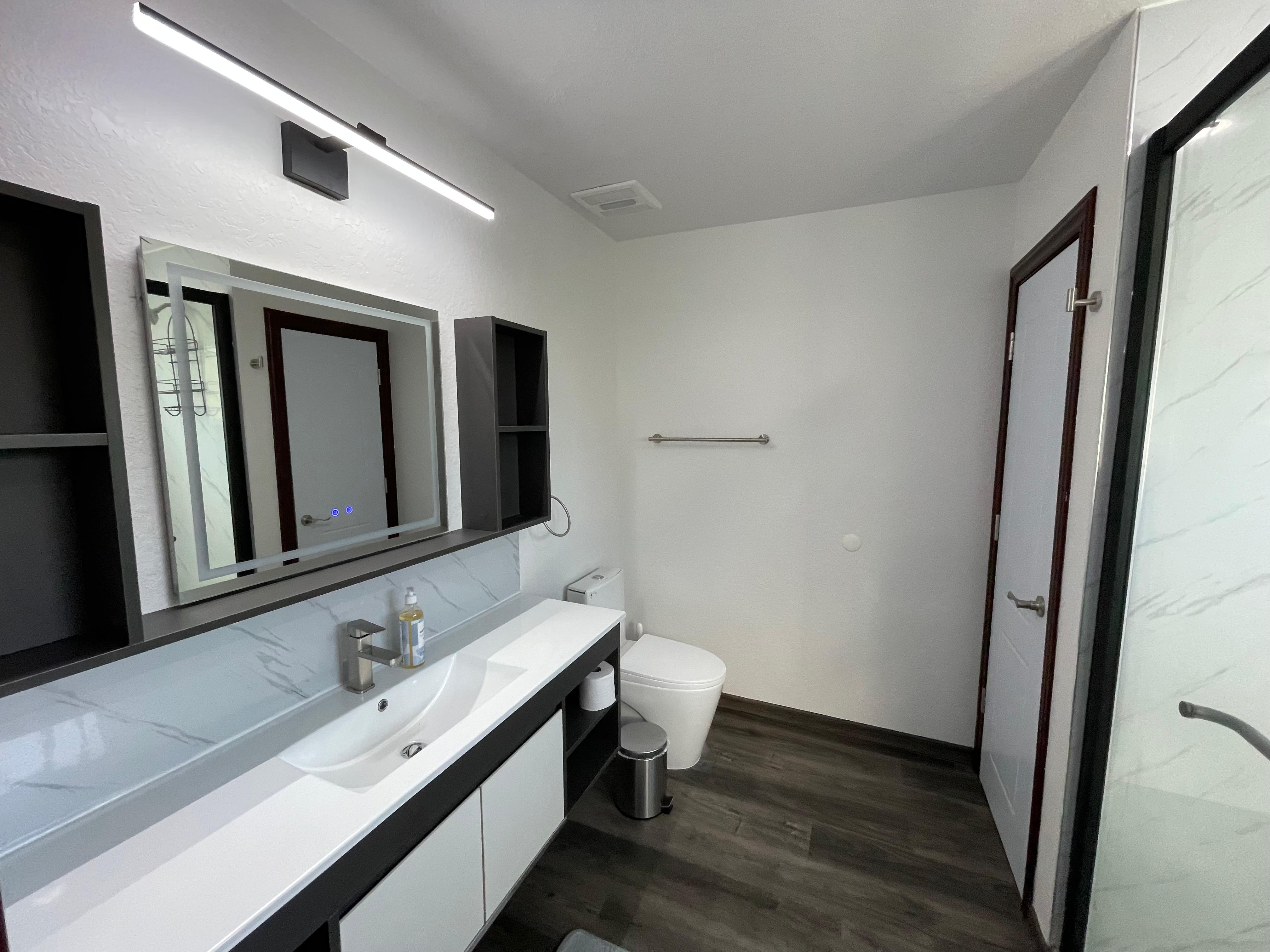 Townhome bathroom with double vanity, large mirrors, toilet, and walk-in shower door