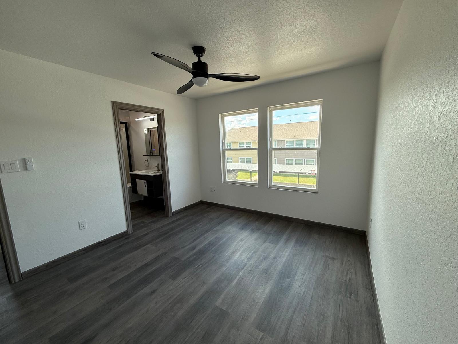 Empty townhome bedroom with two windows, gray flooring, and ceiling fan