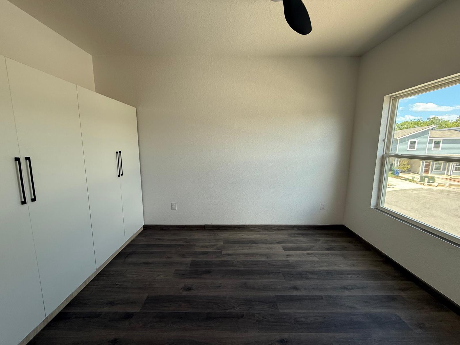 Empty townhome bedroom with built-in white wardrobe cabinets and large window